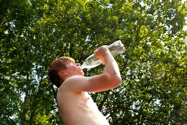 Un jeune garçon boit de l'eau dans une bouteille dans la chaleur — Photo