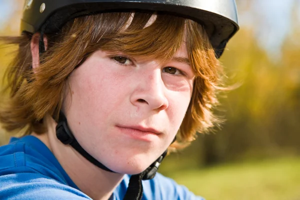 Мальчик с рыжими длинными волосами и шлемом едет на грязном велосипеде и смотрит — стоковое фото