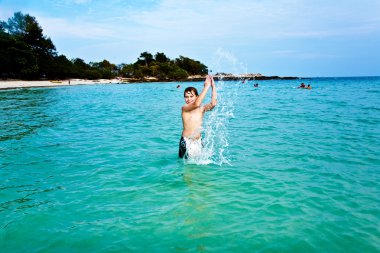 Boy is enjoying the clear warm water at the beautiful beach but clipart