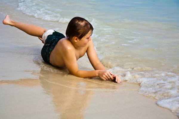 Giovane ragazzo è sdraiato sulla spiaggia e godendo il calore del — Foto Stock