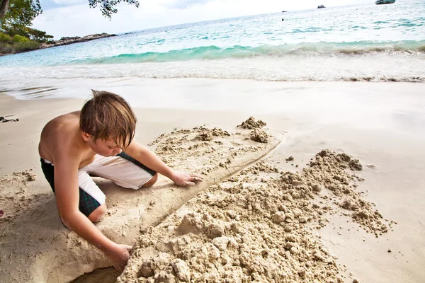 Menino feliz está construindo um canal a partir de areia no bea — Fotografia de Stock