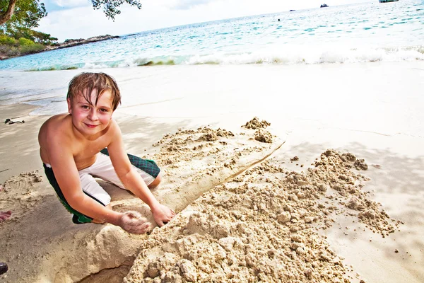 Felice ragazzo sta costruendo un canale di sabbia al bea — Foto Stock