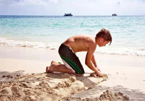 Happy boy is building a canal out of sand at the bea — Stock Photo, Image