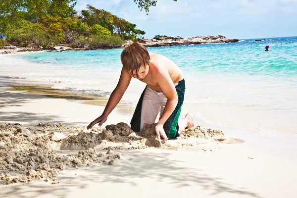 Happy boy is building a canal out of sand at the bea — Stock Photo, Image