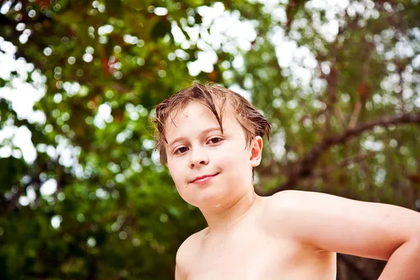 Niño con el pelo mojado sale del mar sonriendo y mira — Foto de Stock