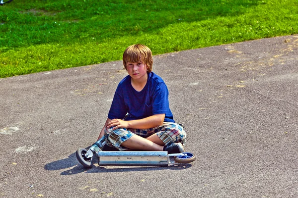 Young boy sitting with his scooter at the ground — Stock Photo, Image