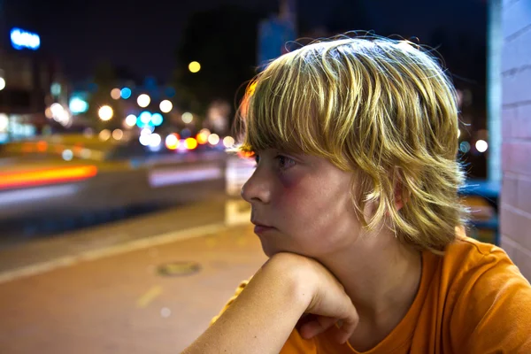 Cute boy smiles tired while sitting outside by night — Stock Photo, Image