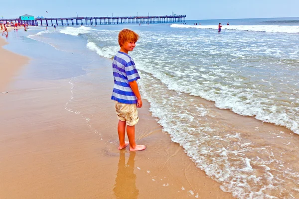 Мальчик прогуливается по пляжу со старым красивым пирсом — стоковое фото