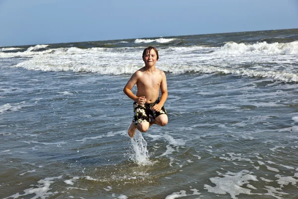 Skoki chłopiec znajduje się piękny ocean falami — Zdjęcie stockowe