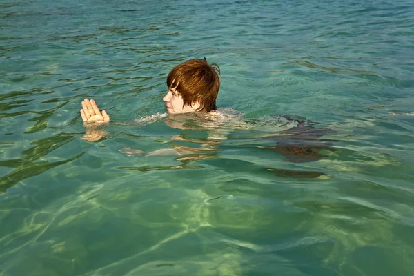 Kızıl saçlı çocuk güzel denizde bir köpekbalığını taklit eder. — Stok fotoğraf