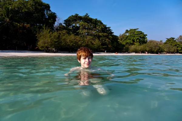 Ragazzo con i capelli rossi sta nuotando in bella spiaggia calda e limpida come — Foto Stock