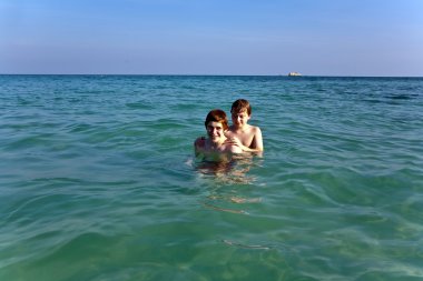 Brothers are enjoying the clear warm water at the beautiful beac clipart