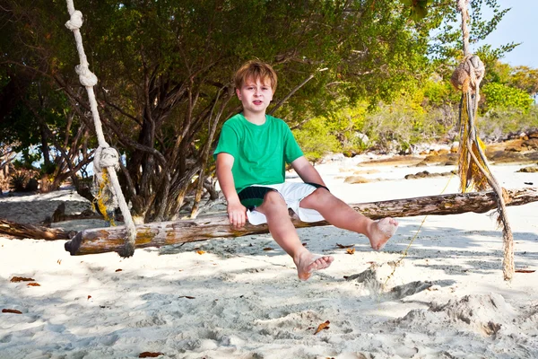Chłopiec siedzi na huśtawce na plaży w cieniu drzew — Zdjęcie stockowe