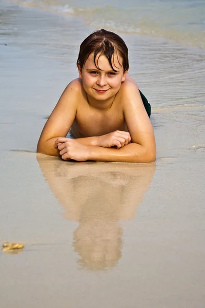 Niño está tumbado en la playa y disfrutando de la calidez de la —  Fotos de Stock