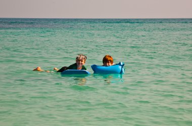 Children are swimming and using an air-matress for relaxing at the clear se clipart