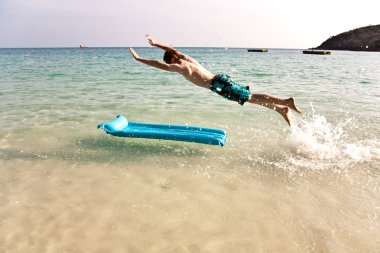 Young boy with red hair in swimsuit is running along the beautif clipart