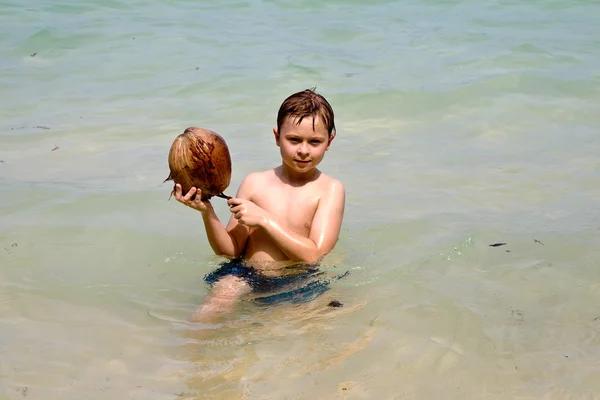 Chico está jugando con un coco en una hermosa playa — Foto de Stock