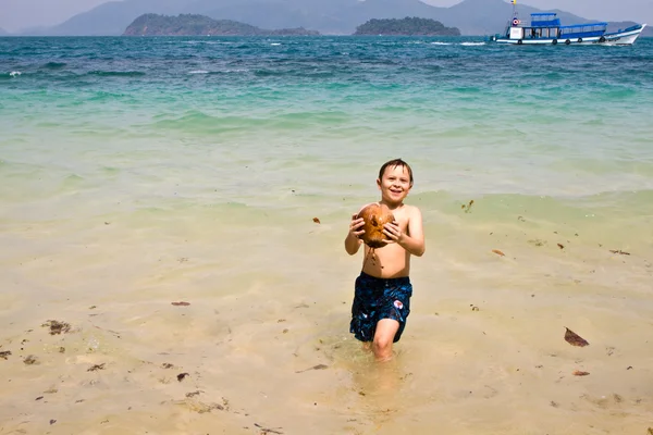 Junge spielt an einem schönen Strand mit einer Kokosnuss — Stockfoto