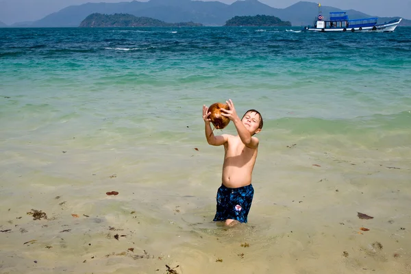 Jongen speelt met een kokosnoot op een prachtig strand — Stockfoto