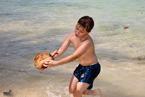 Хлопчик грає з кокосовим горіхом на красивому пляжі — стокове фото