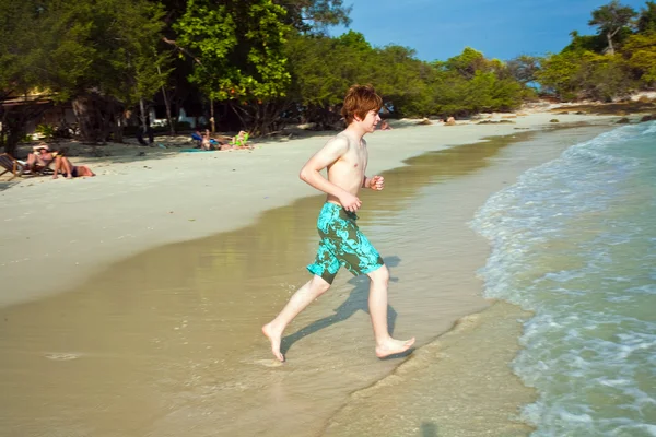 Young boy with red hair in swimsuit is running along the beautif — Stock Photo, Image
