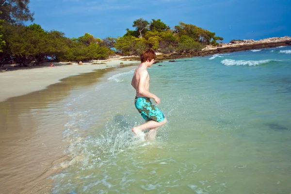 Niño con el pelo rojo en traje de baño se ejecuta a lo largo de la hermosa playa —  Fotos de Stock