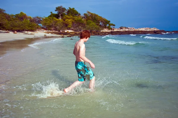 Niño con el pelo rojo en traje de baño está corriendo a lo largo de la hermosa playa un —  Fotos de Stock