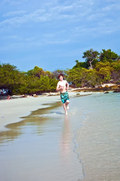 Niño con el pelo rojo en traje de baño se ejecuta a lo largo de la hermosa playa —  Fotos de Stock
