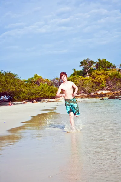 Молодий хлопчик з рудим волоссям у купальнику біжить уздовж прекрасного пляжу — стокове фото