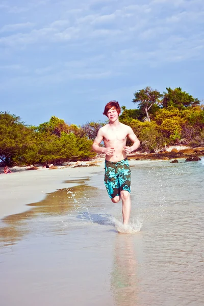 Young boy with red hair in swimsuit is running along the beautiful beach — Stock Photo, Image