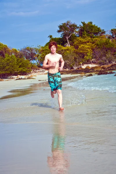 Kleiner Junge mit roten Haaren im Badeanzug läuft am schönen Strand entlang — Stockfoto