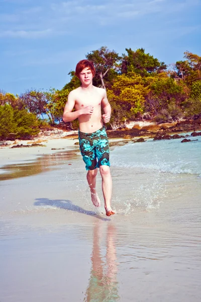 Mladík s červenými vlasy v plavkách je spuštěn na nádherné pláži — Stock fotografie