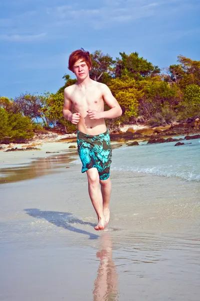 穿泳衣的红头发的小男孩正在运行沿美丽的海滩 — 图库照片