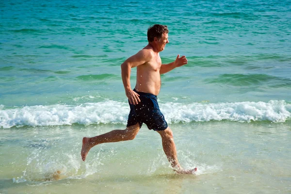 Az ember a gyönyörű strand mentén fut. — Stock Fotó
