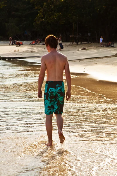 Giovane ragazzo sta camminando lungo la bella spiaggia in controluce — Foto Stock