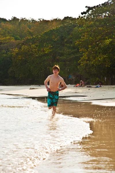 Jonge jongen loopt langs het prachtige strand in achtergrondverlichting — Stockfoto