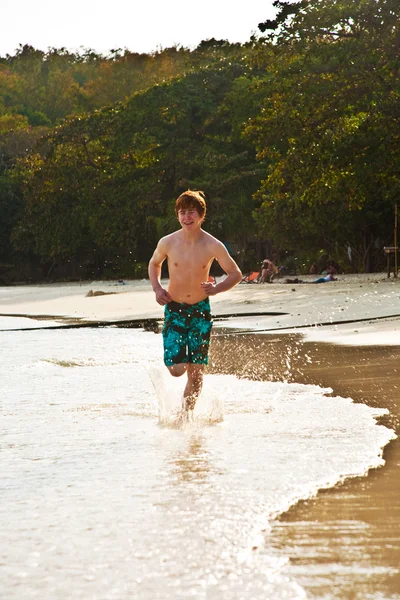 Jonge jongen loopt langs het prachtige strand in achtergrondverlichting — Stockfoto