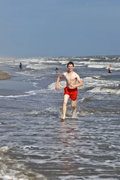 Chico corriendo a lo largo de la hermosa playa en las olas —  Fotos de Stock