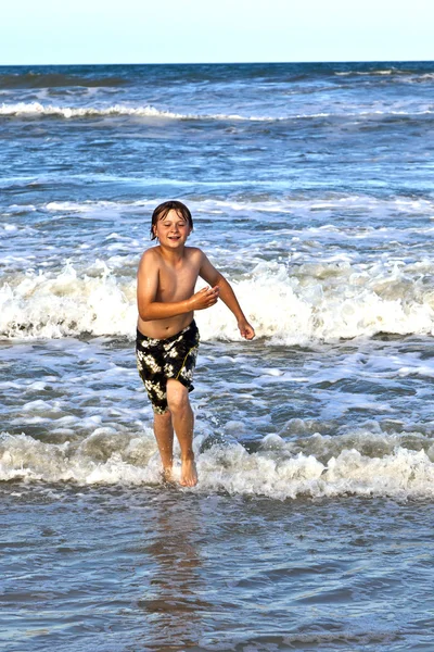 Niño corriendo a través del agua en la playa — Foto de Stock