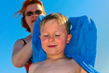 Mother with red hair and sunglasses helps her son to dry with a clipart