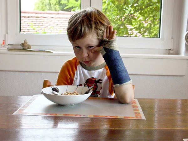 Pojke på frukost med gjutna på sin brutna arm — Stockfoto