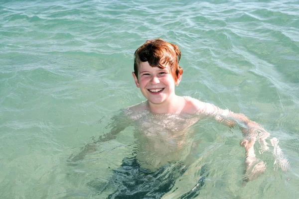 Niño con el pelo rojo está nadando en el mar y lo disfruta y sonríe —  Fotos de Stock