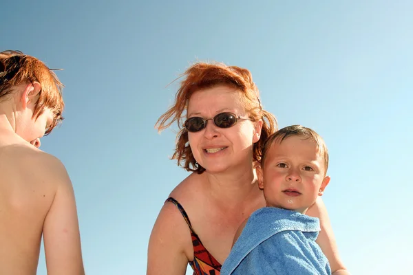 Madre con pelo rojo y gafas de sol ayuda a su hijo a secarse con un —  Fotos de Stock