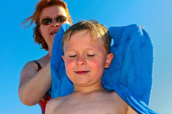 Madre con pelo rojo y gafas de sol ayuda a su hijo a secarse con un — Foto de Stock
