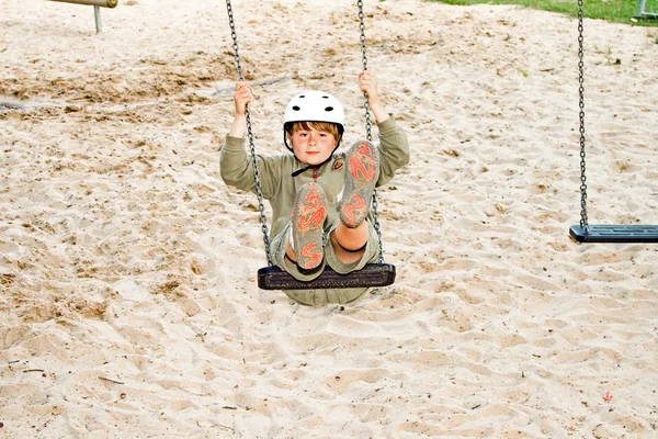 Boy on a swing is wearing a helmet and enjoys it — Stock Photo, Image
