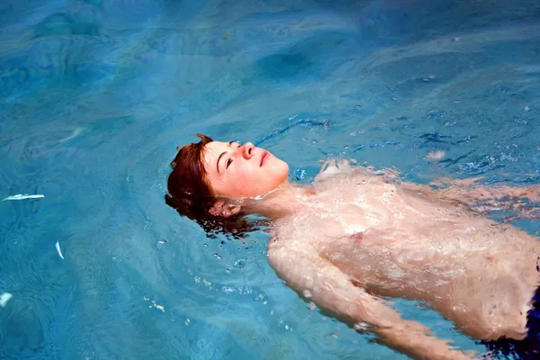 Jongen met rood haar enyoing zwemmen in een overdekt zwembad en leugenachtige o — Stockfoto
