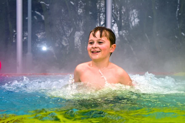 Menino se diverte na piscina térmica ao ar livre no inverno — Fotografia de Stock