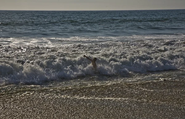 Fare il bagno al tramonto tra le onde sulla spiaggia — Foto Stock