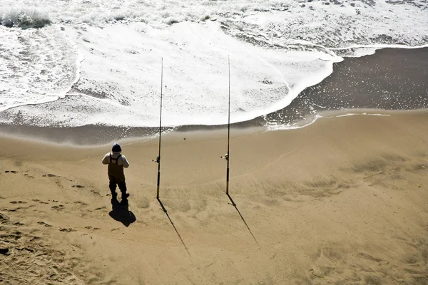 Рыбак на пляже с двумя стержнями — стоковое фото