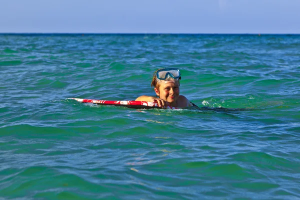 Jovem rapaz rasteja com a prancha de surf através do mar — Fotografia de Stock